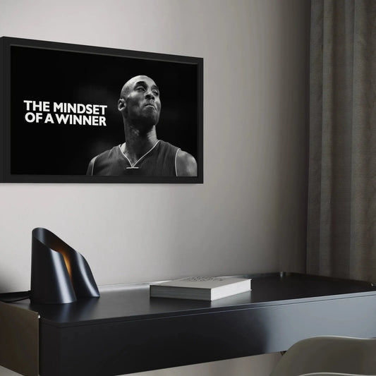 Framed poster with a person's portrait and text 'The Mindset of a Winner' on a wall above a desk.