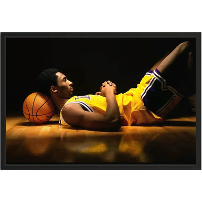 Close framed product shot of a basketball player in a yellow jersey resting on the court with a ball under his head on a black backdrop.