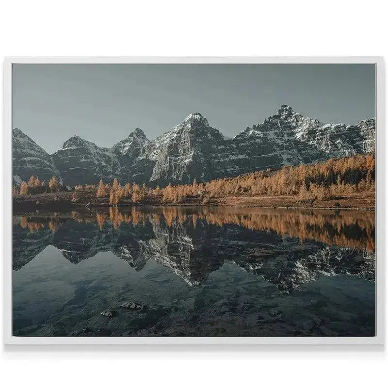 High-angle view highlighting the snowline and jagged peaks towering Above the Larches, contrasting with the warm foliage.