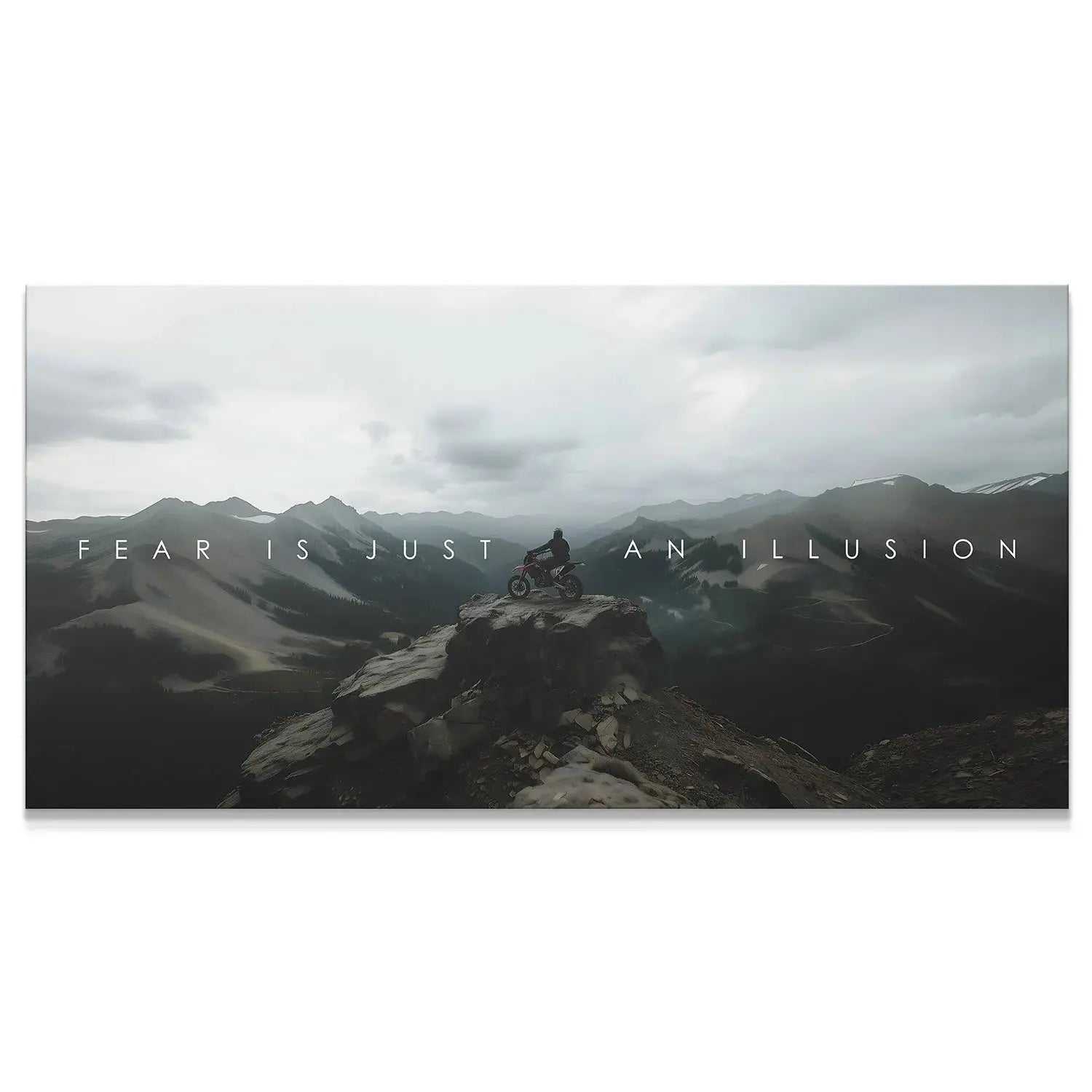 Wide panoramic view of the biker on the remote mountain peak, emphasizing the quote 'Action Sports - Fear Is Just An Illusion.'