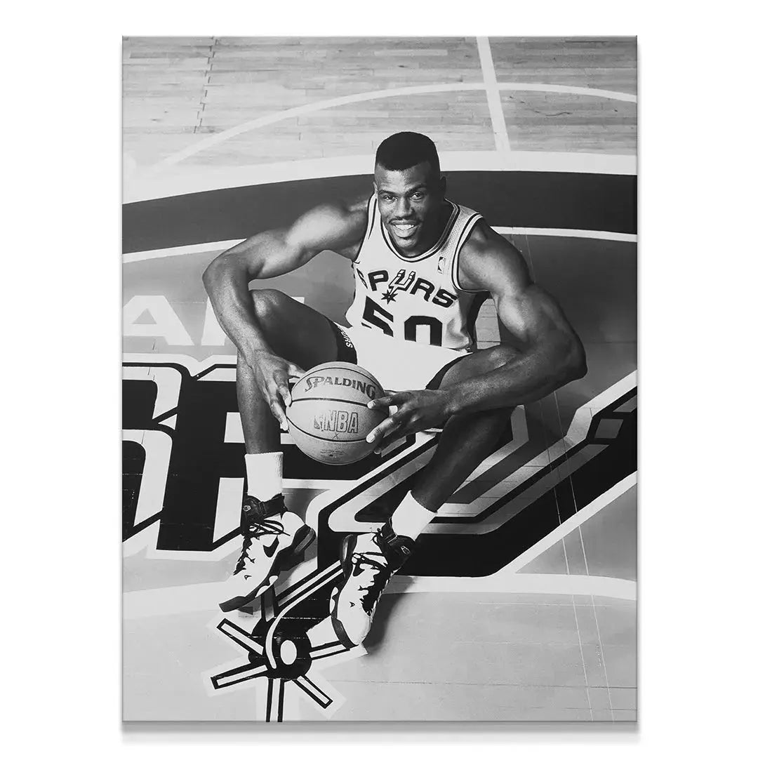 Black and white professional basketball portrait of David Robinson - #1 sitting mid-court, holding a Spalding ball.