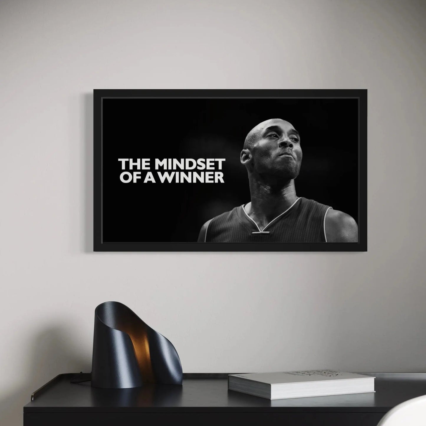 Framed poster with a black and white image of a person and text 'The Mindset of a Winner' on a wall above a desk.