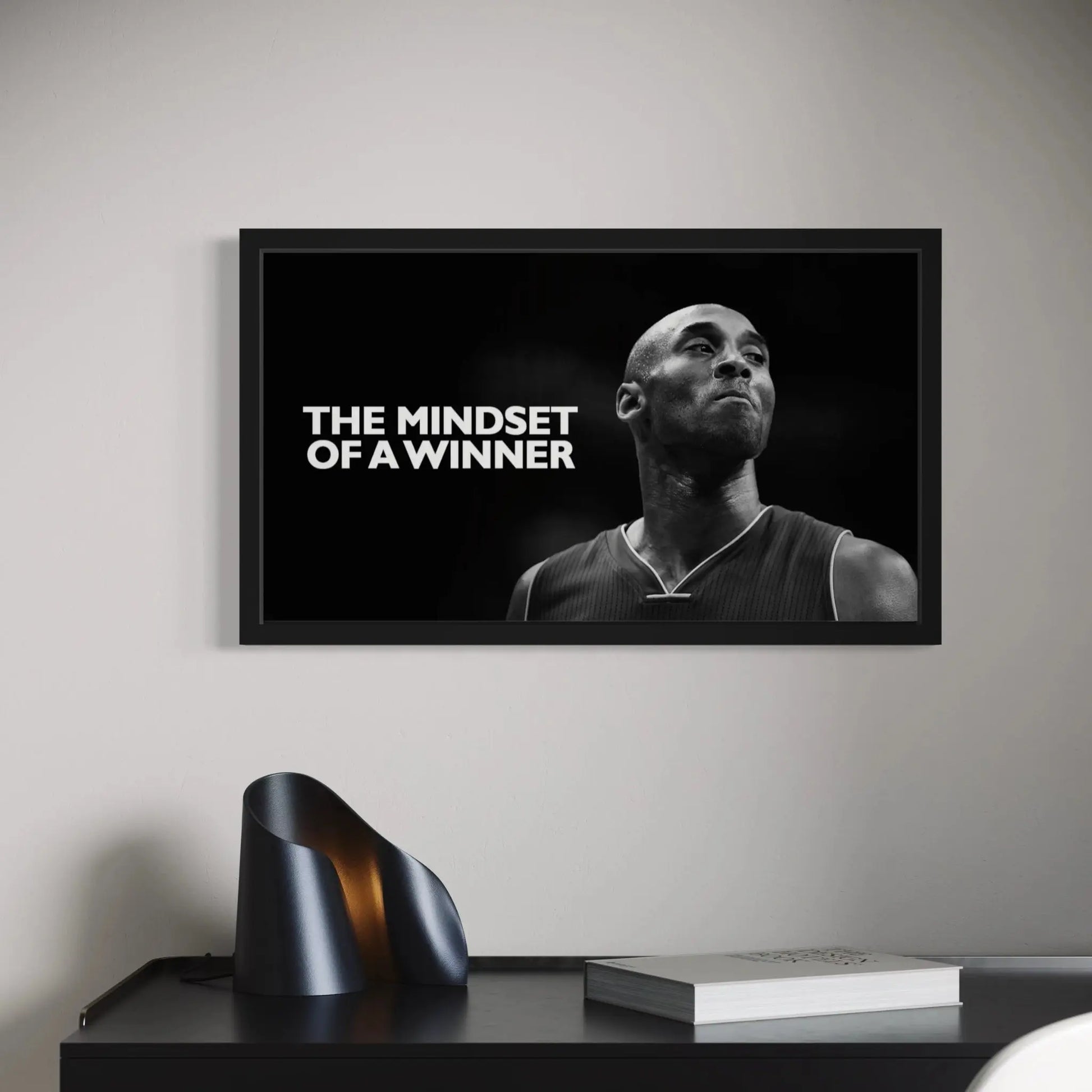 Framed poster with a black and white image of a person and text 'The Mindset of a Winner' on a wall above a desk.