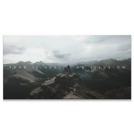 Wide panoramic view of the biker on the remote mountain peak, emphasizing the quote 'Action Sports - Fear Is Just An Illusion.'