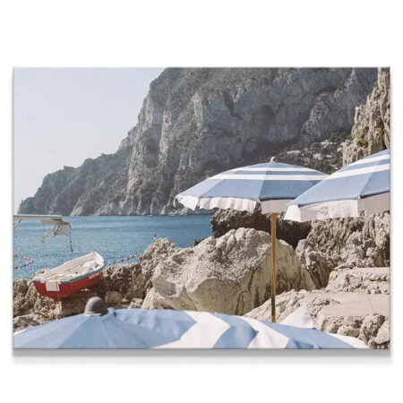 Rocky beach shoreline view of Capri with blue and white striped umbrellas.