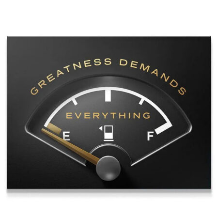 Close-up view of the metallic needle pointing to 'E' which stands for 'Everything' on the 'Greatness Demands Everything' gauge.