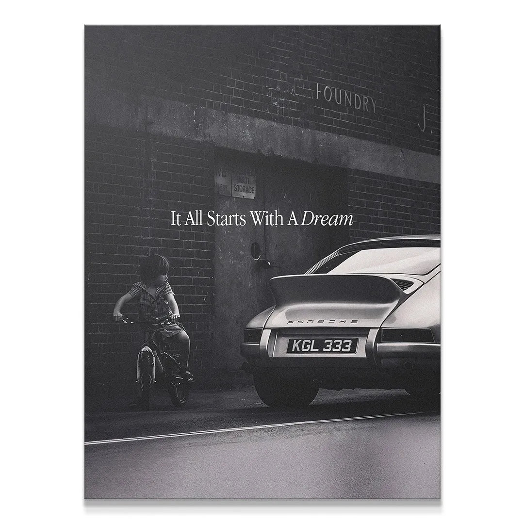 Monochrome art print showing a child on a bicycle near a classic Porsche; It All Starts With A Dream quote visible on the brick wall.