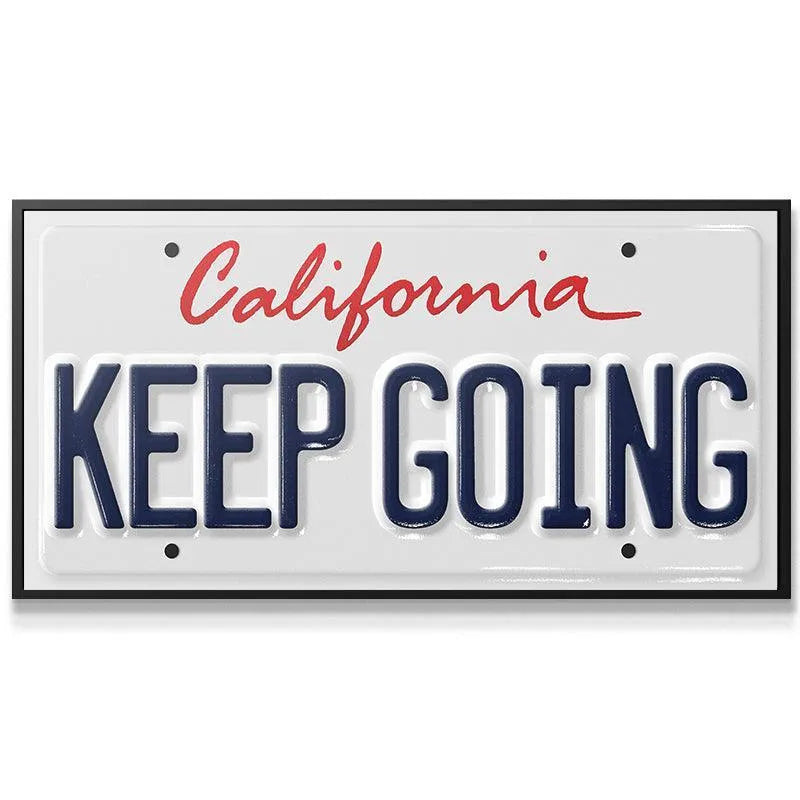 Close-up of the embossed blue text "KEEP GOING" on the 'Keep Going - CA' sign showing texture.