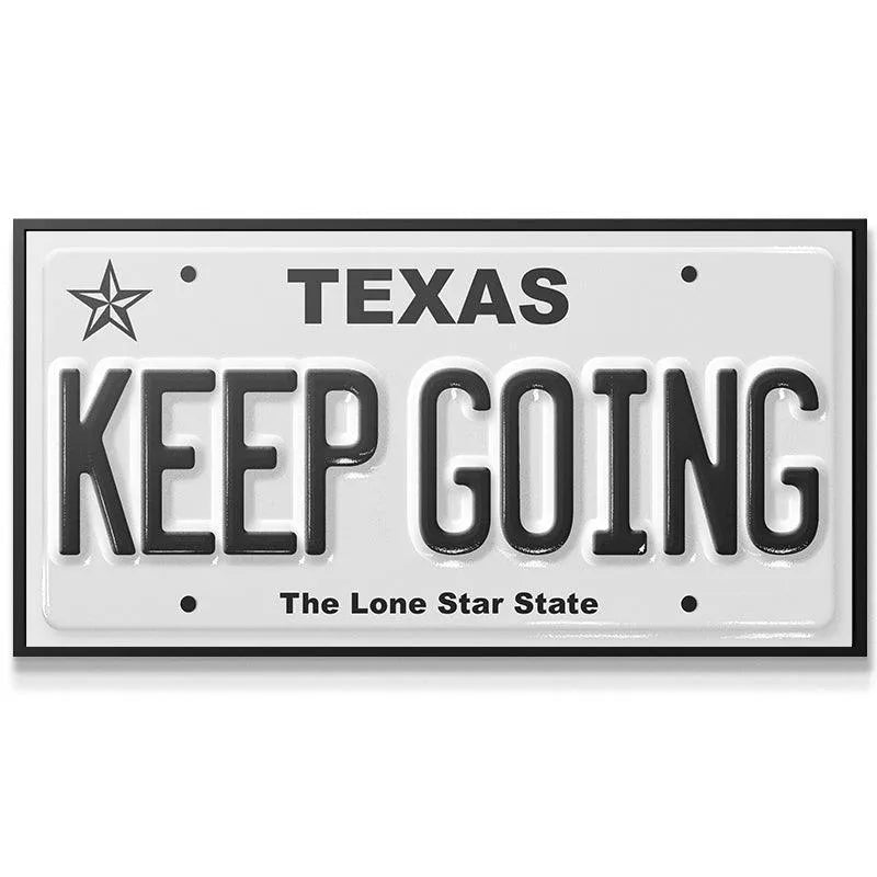 Close-up detail of the raised lettering and star emblem on the 'Keep Going - TX' license plate replica.