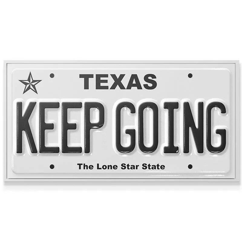 Angled shot highlighting the glossy white finish and black 3D text of the 'Keep Going - TX' novelty plate.