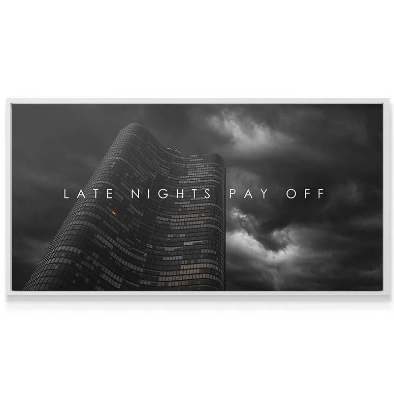 Wide shot of the motivational wall art 'Late Nights Pay Off' centered in a minimalist, ambitious office environment.