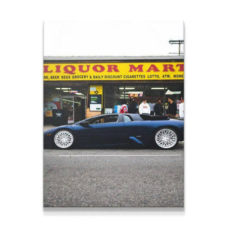 Full side profile of lowered blue Lamborghini Murciélago parked in front of the yellow-signed Liquor Mart Murcielago.
