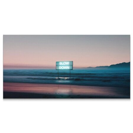 Wide landscape shot of the beach at twilight featuring the glowing 'Slow Down' neon sign installation.