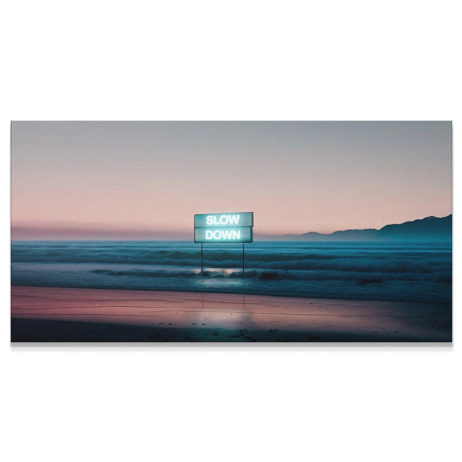 Wide landscape shot of the beach at twilight featuring the glowing 'Slow Down' neon sign installation.