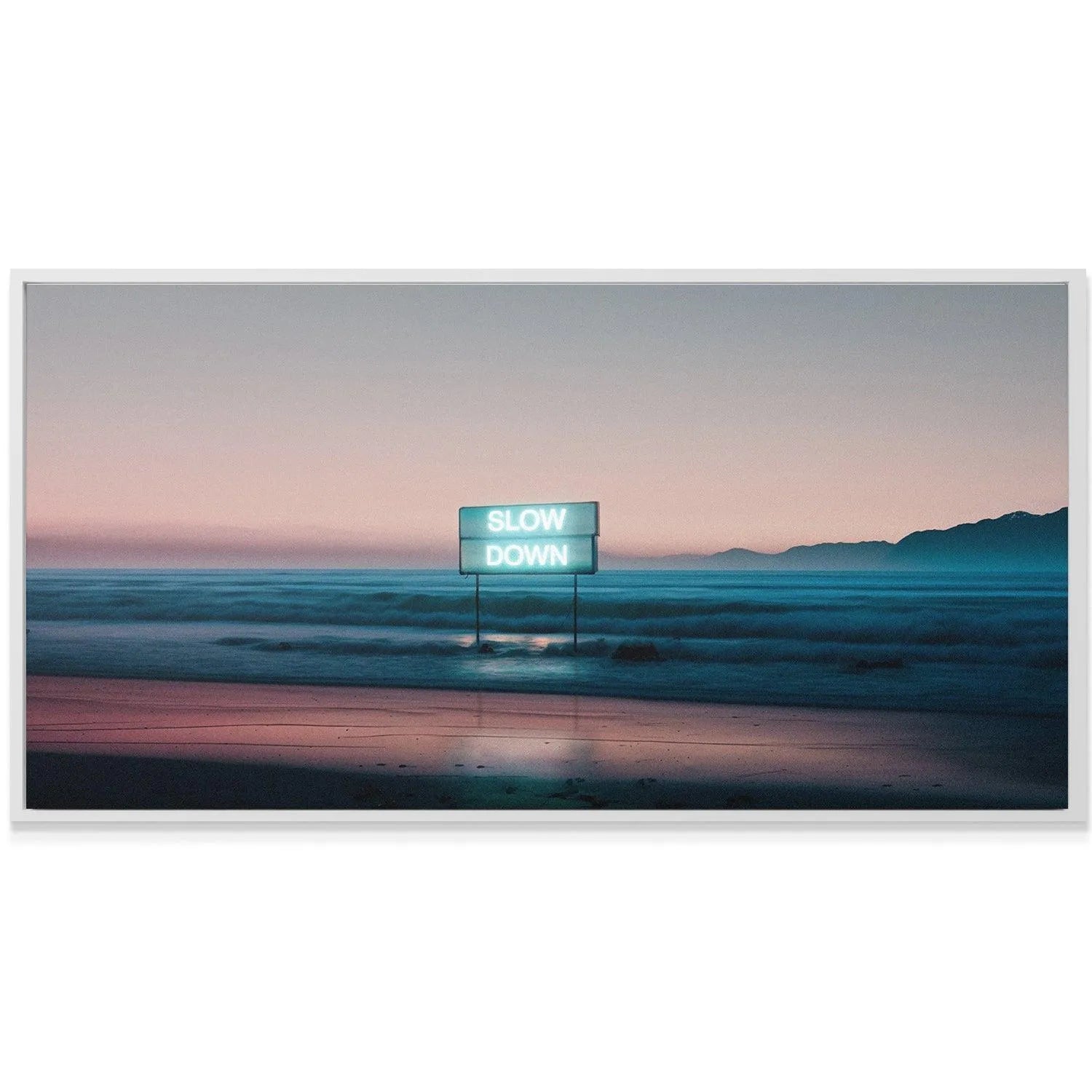 Long-exposure angle capturing the smooth, misty ocean waves near the 'Slow Down' sign on the shore.