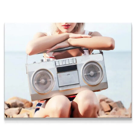 Woman holding vintage silver boombox on sunlit beach rocks, fulfilling her ultimate Speaker Duty.