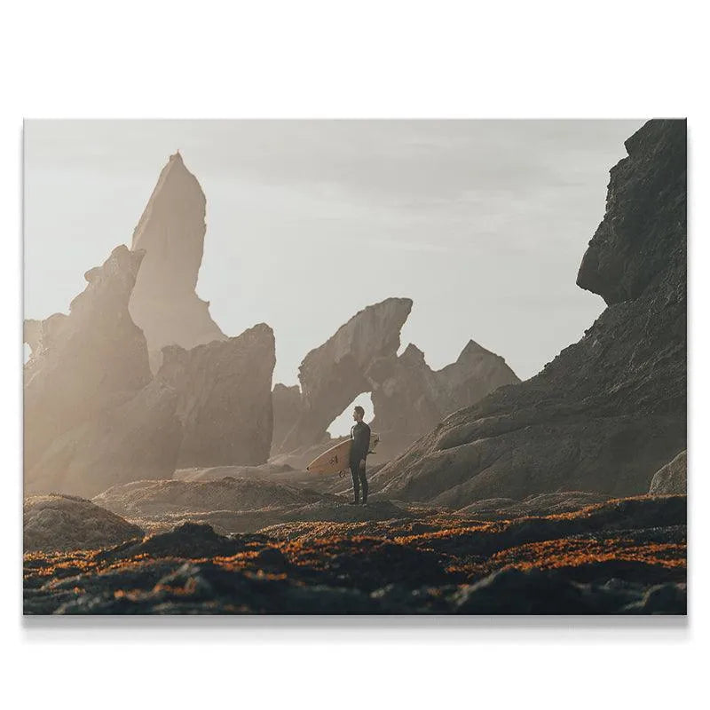 Rugged coastal landscape featuring the Swell Watcher surfer holding a board amidst giant rock formations.