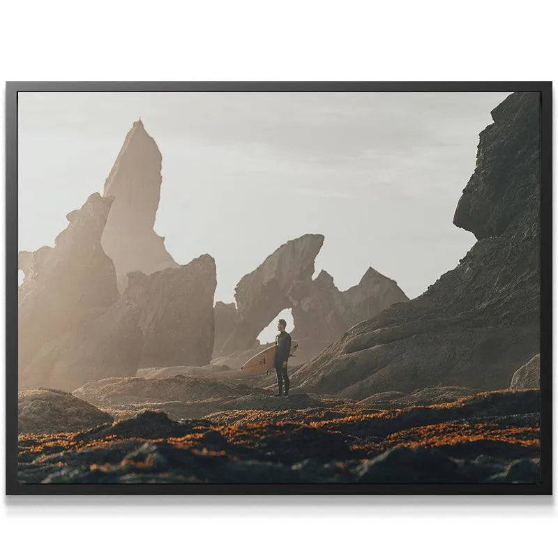 Low-angle view highlighting the massive scale of the cliffs above the Swell Watcher figure on the shore.