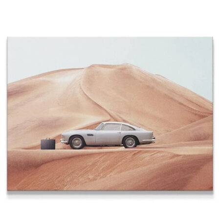 Wide shot of classic silver sports car and black briefcase against massive sand dunes captured in 'The Drop' print.