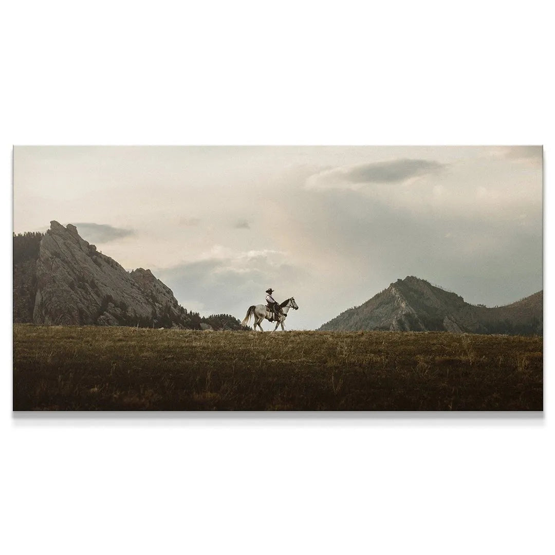 Panoramic view of The Lone Rider crossing dry plains before rugged, rocky mountains.