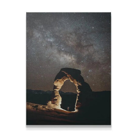 Full shot of Delicate Arch illuminated at night 'Under the Arch Skies', showing the Milky Way overhead.